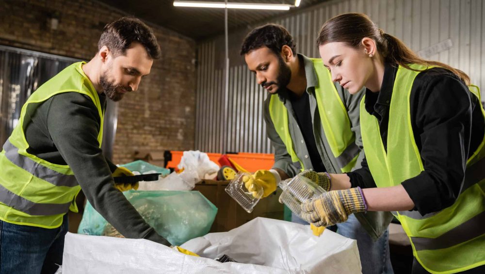 Interracial sorters in protective gloves and safety vests taking plastic containers from sacks while